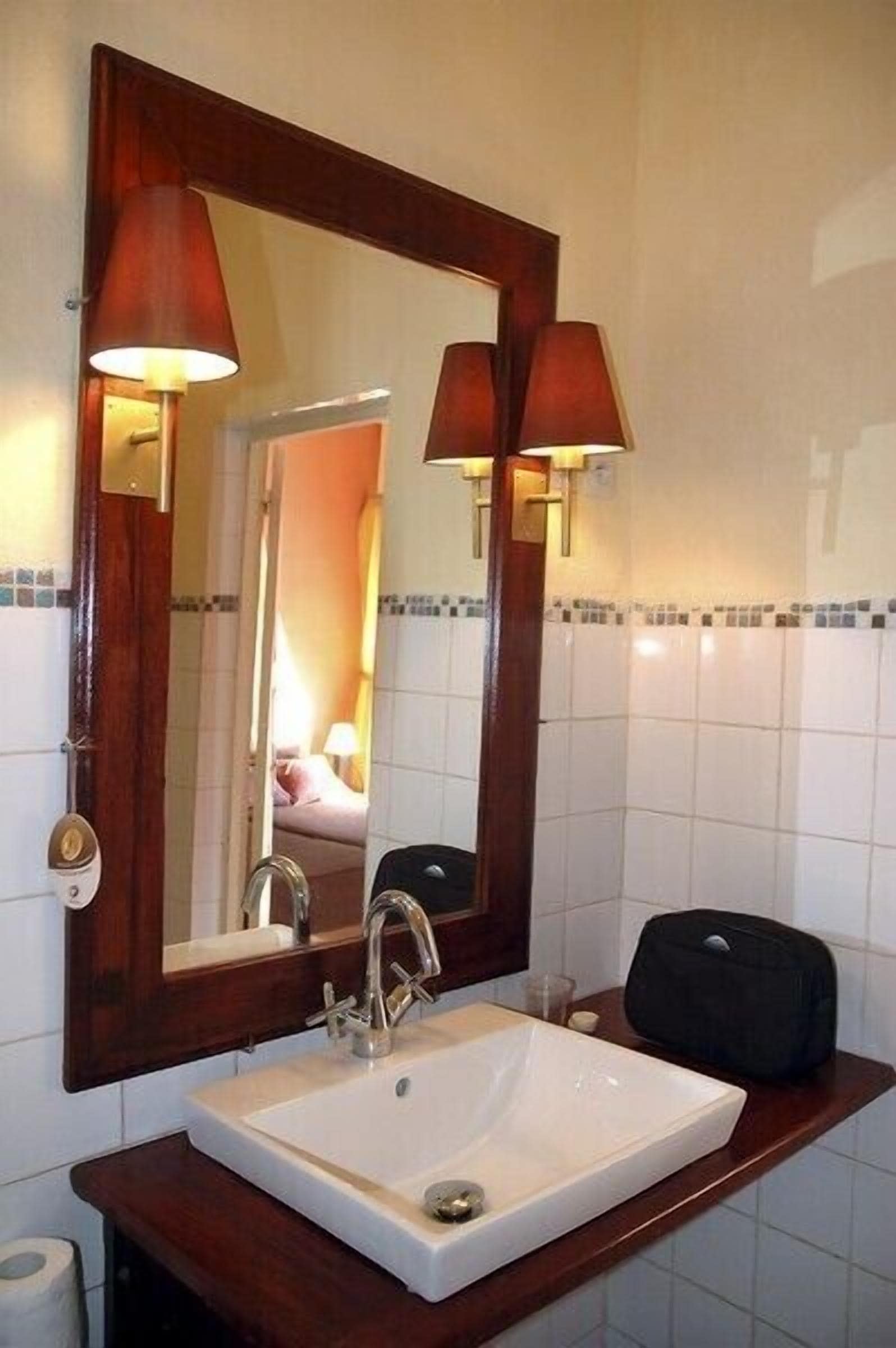 Een badkamer met een grote spiegel, twee wandlampen, een wit wastafel en een houten opbergmeubel.