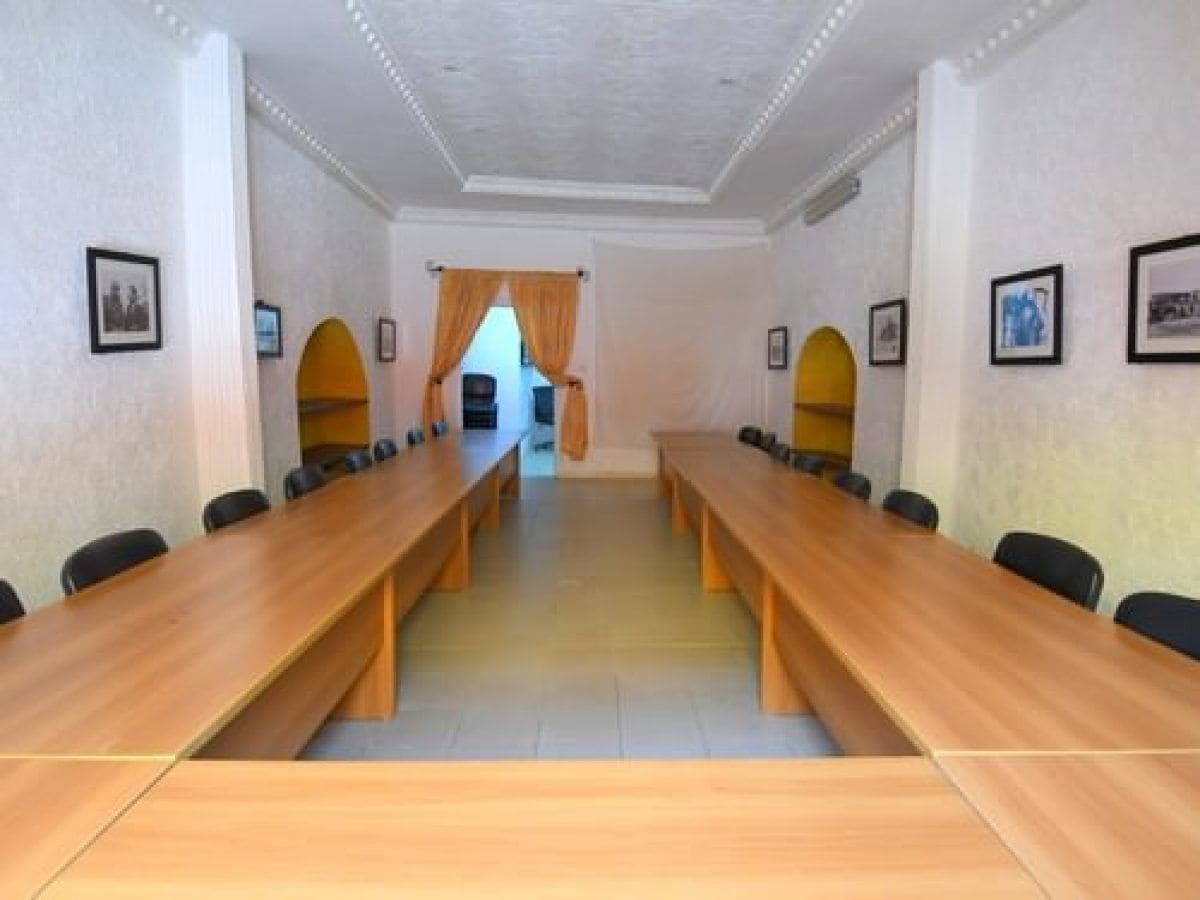 Une salle de conférence avec une longue table en bois, des chaises noires et des tableaux encadrés accrochés aux murs.