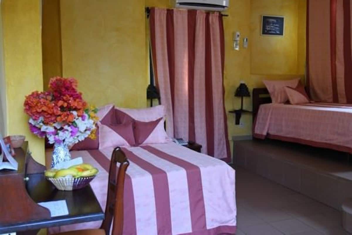 A hotel room with a bed, a desk with a vase of flowers, and a chair.