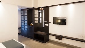 A modern hotel room with a flat-screen TV mounted on the wall, a built-in bench, and a sliding door leading to a closet. - Copper Folia (Kozhikode)