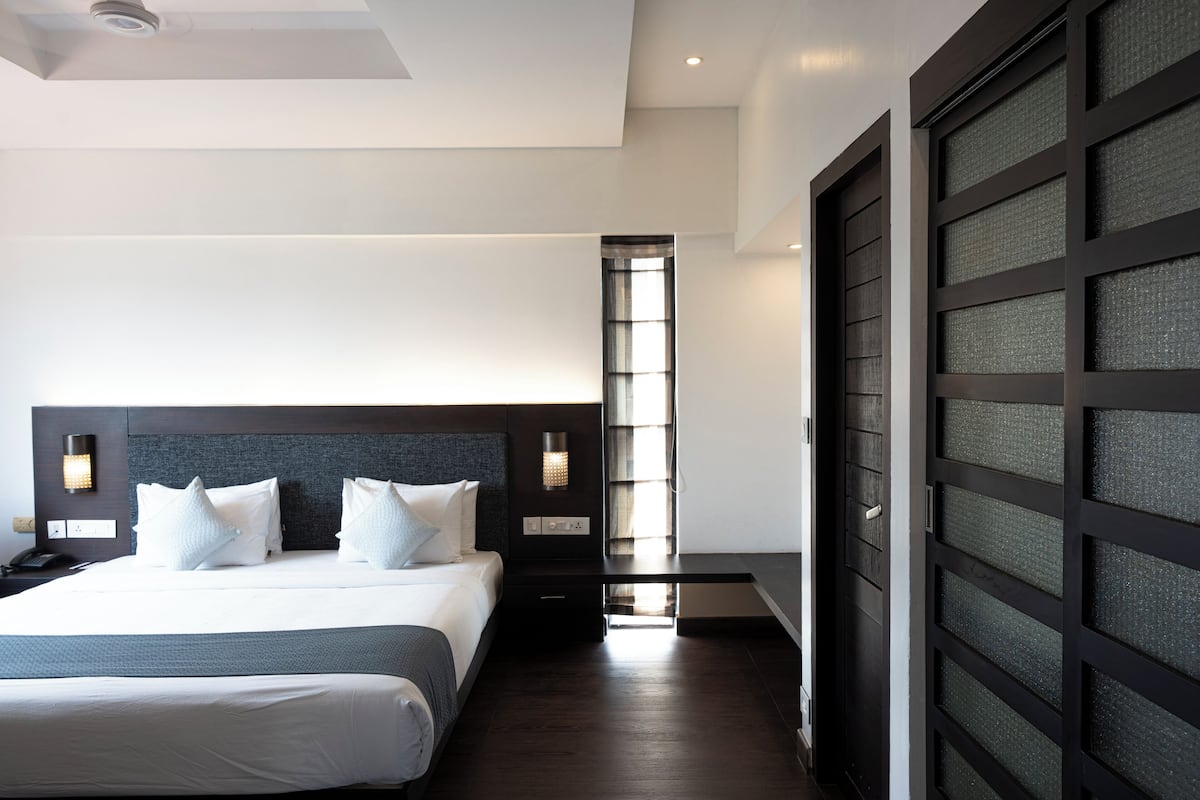 A modern hotel room with a large bed, a nightstand, a desk, and a view of the city through a window.