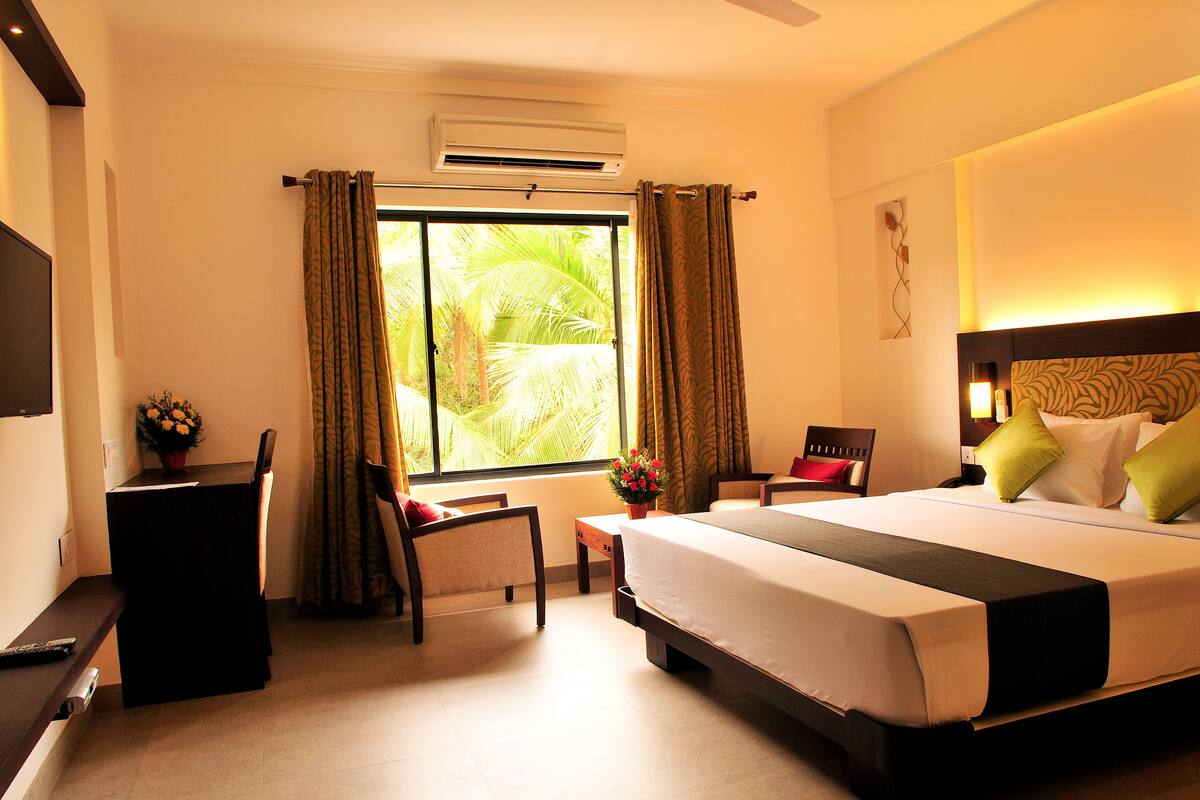 A hotel room with a large bed, a desk, a chair, and a window with curtains.