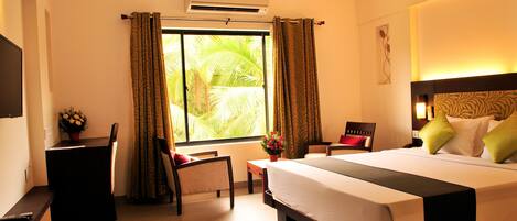 A hotel room with a large bed, a desk, a chair, and a window with curtains.