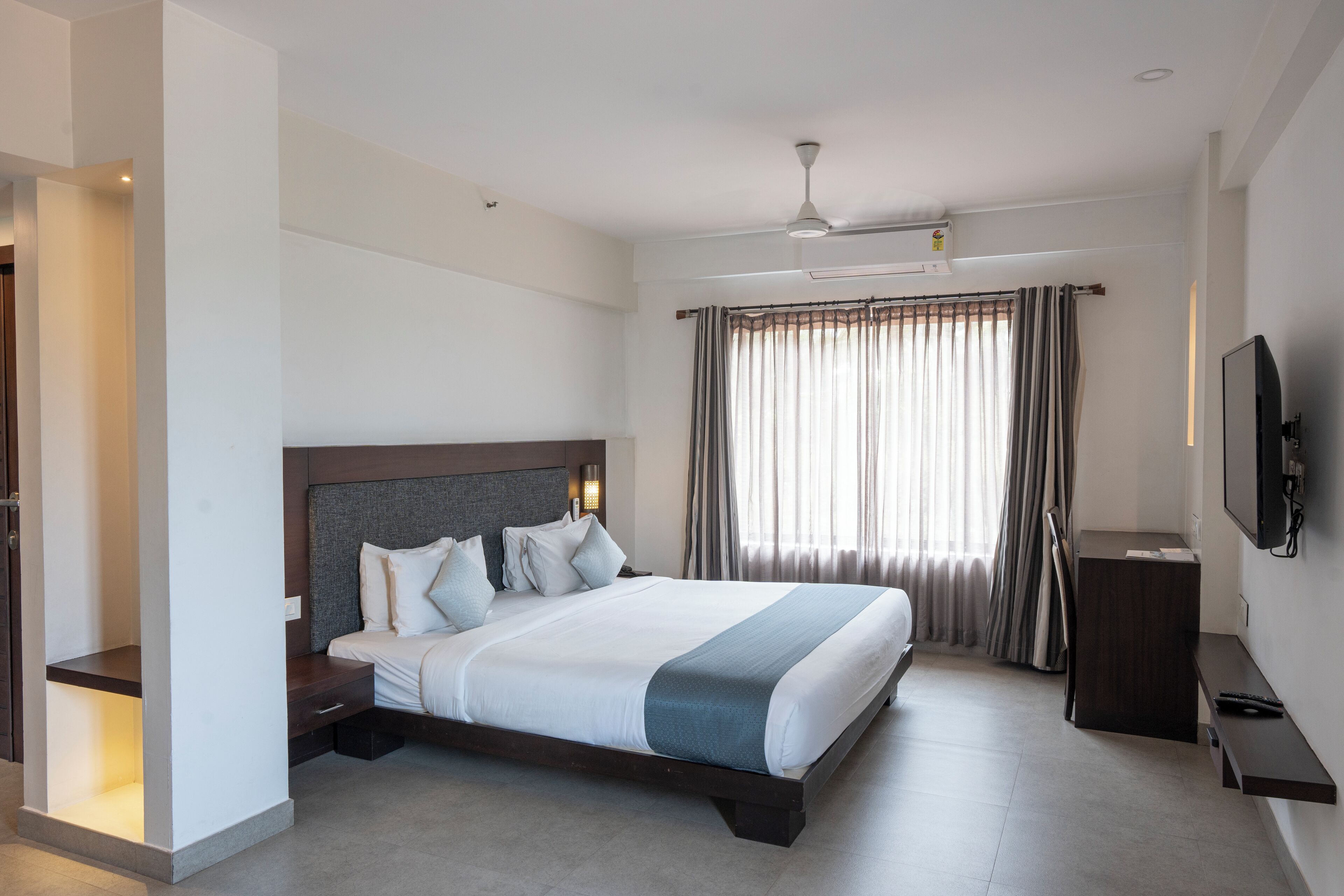 A modern hotel room with a large bed, a desk, a flat-screen TV, and a ceiling fan.