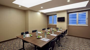 A conference room with a long table, chairs, water bottles, and a flat-screen TV.