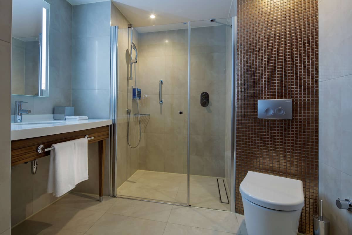A modern bathroom with a glass-enclosed shower, a white toilet, and a wooden vanity with a towel hanging.