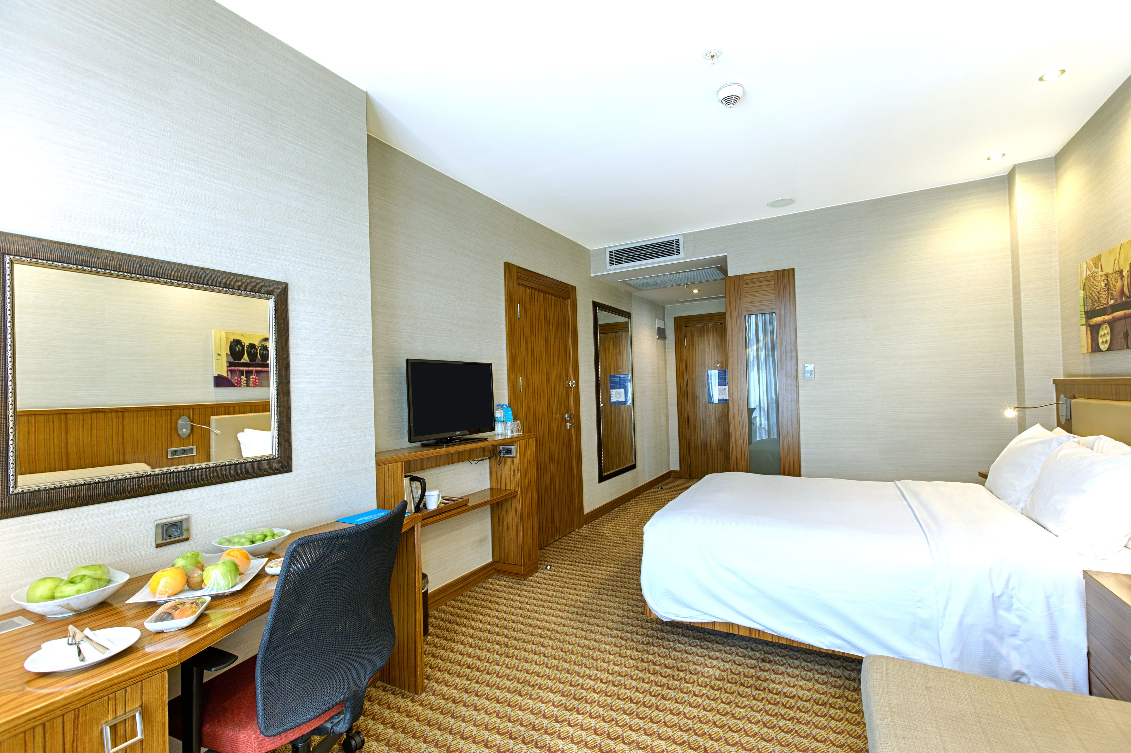 Habitación de hotel con cama, escritorio con computadora, espejo y televisión.