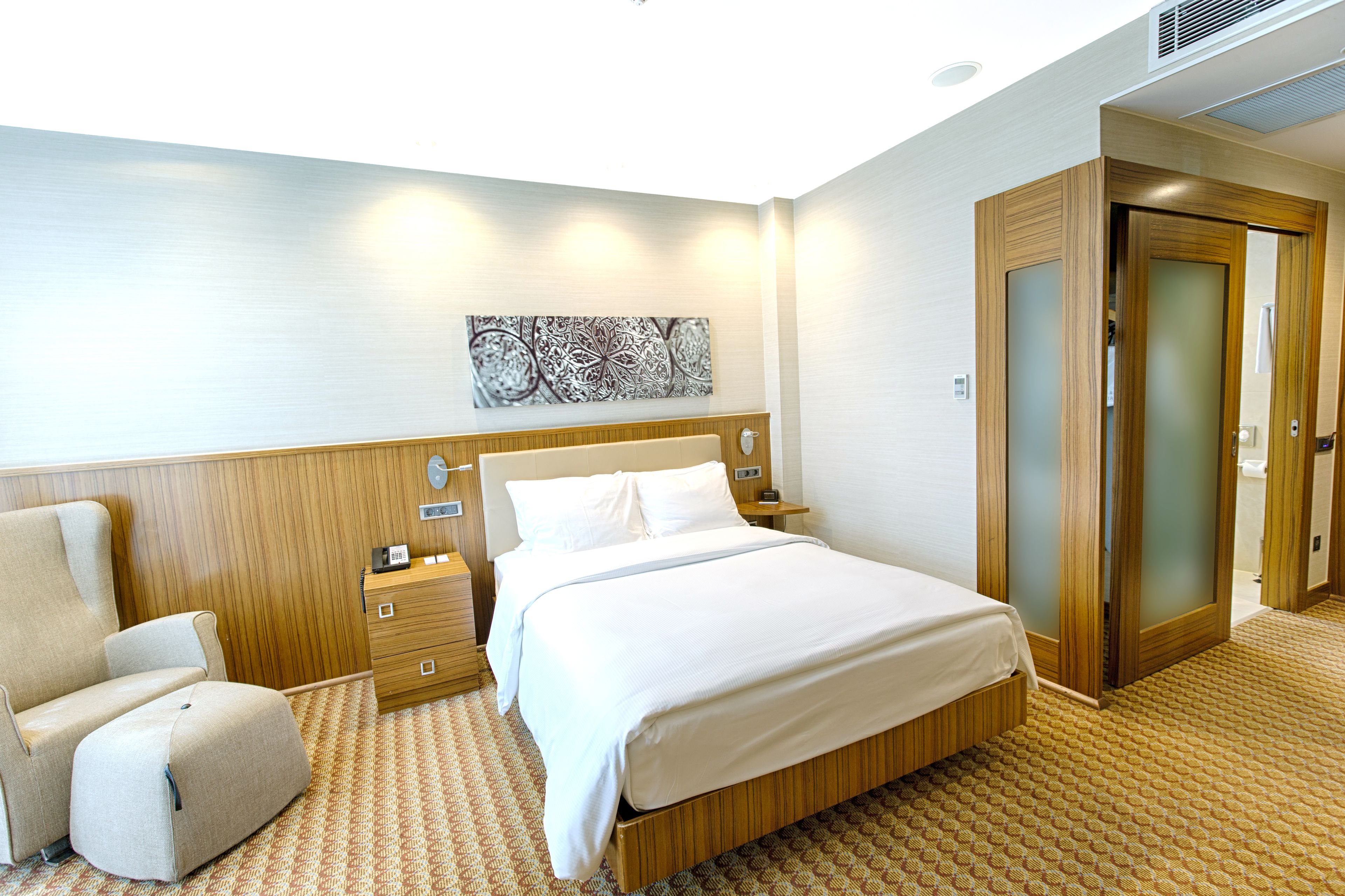 A hotel room with a bed, a chair, a nightstand, and a wooden wardrobe.
