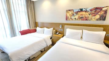Hotelkamer met twee bedden, een houten hoofdbord, een nachtkastje met telefoon en een groot raam met gordijnen.