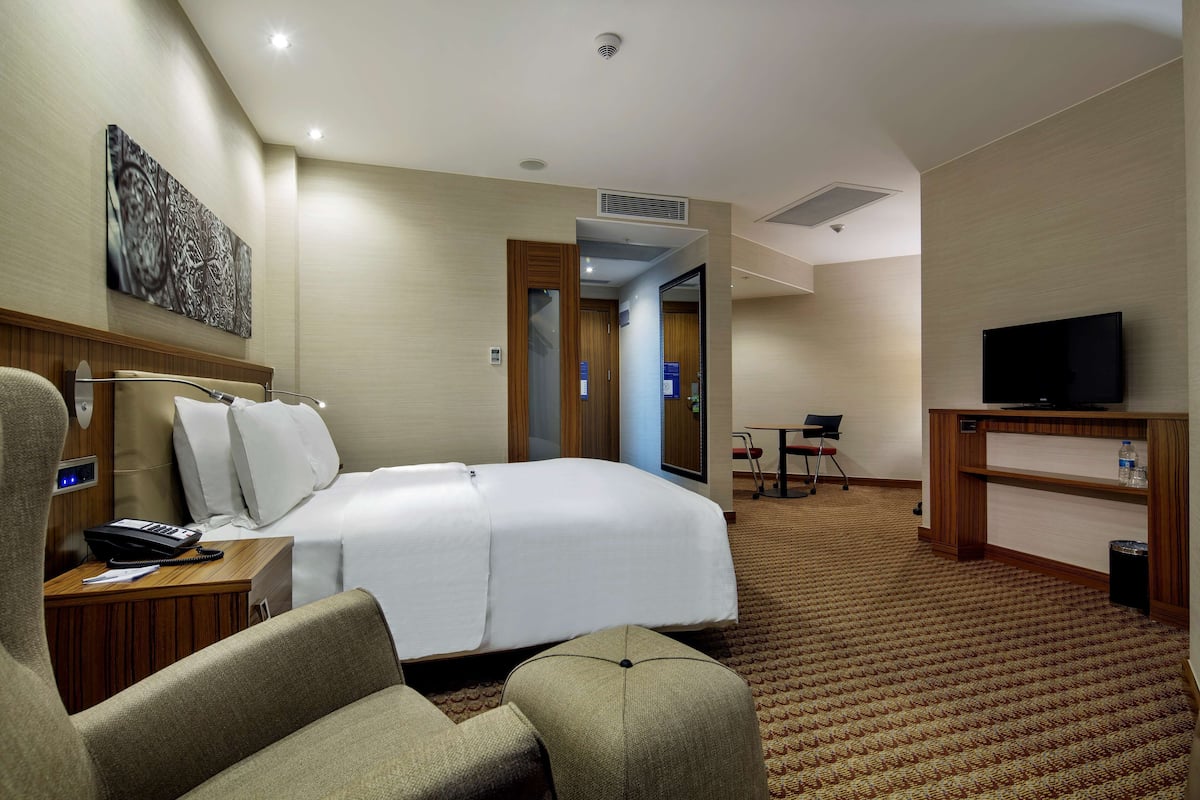 A hotel room with a bed, a desk, a chair, a television, and a painting on the wall.