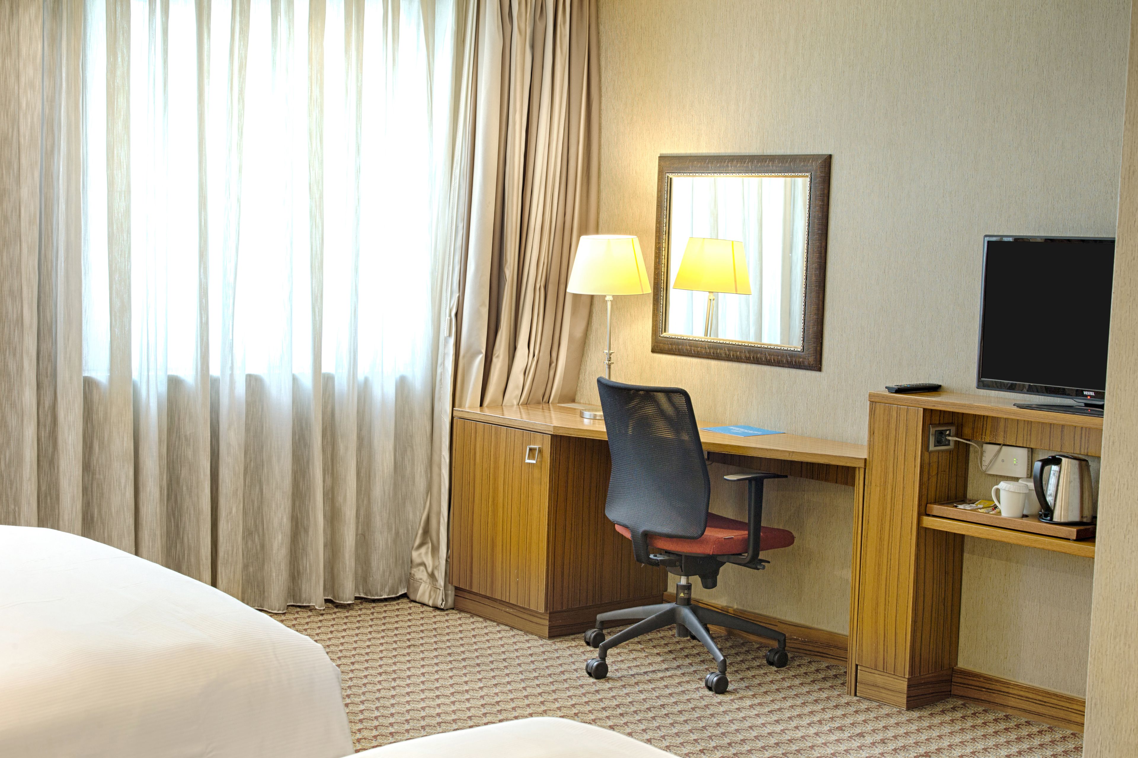 Una habitación de hotel con cama, escritorio, silla, lámpara, televisor y cafetera.