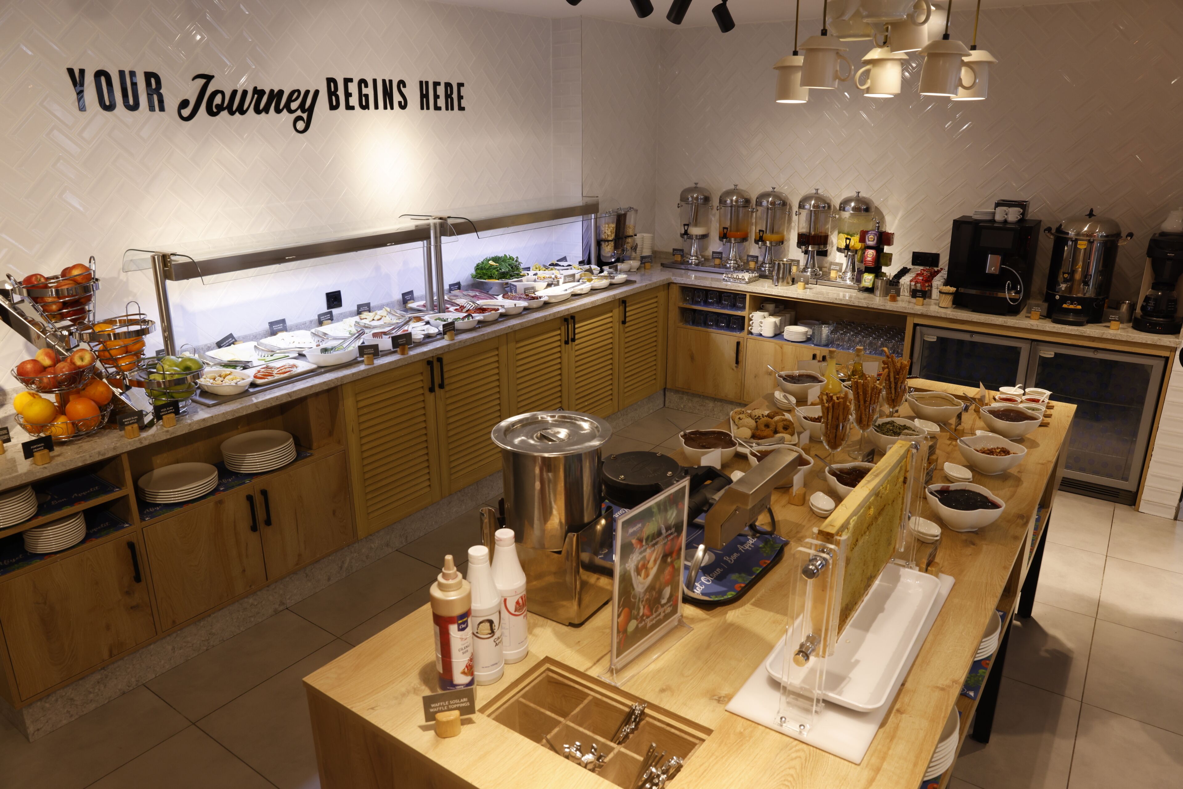A buffet setup with various food items, a coffee station, and a sign that reads 'YOUR Journey Begins Here.'