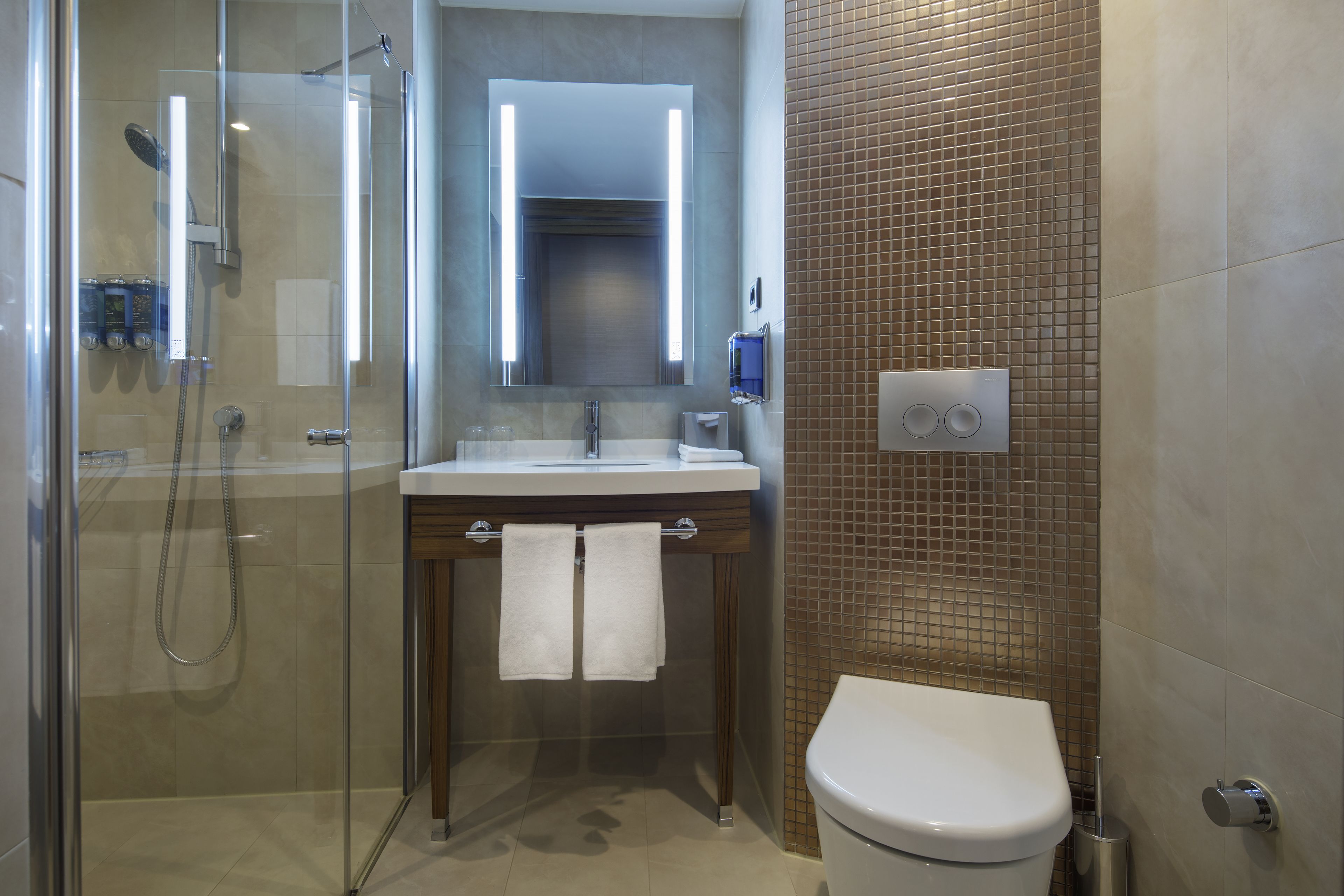 Un baño moderno con ducha de vidrio, un lavabo con espejo y un inodoro.