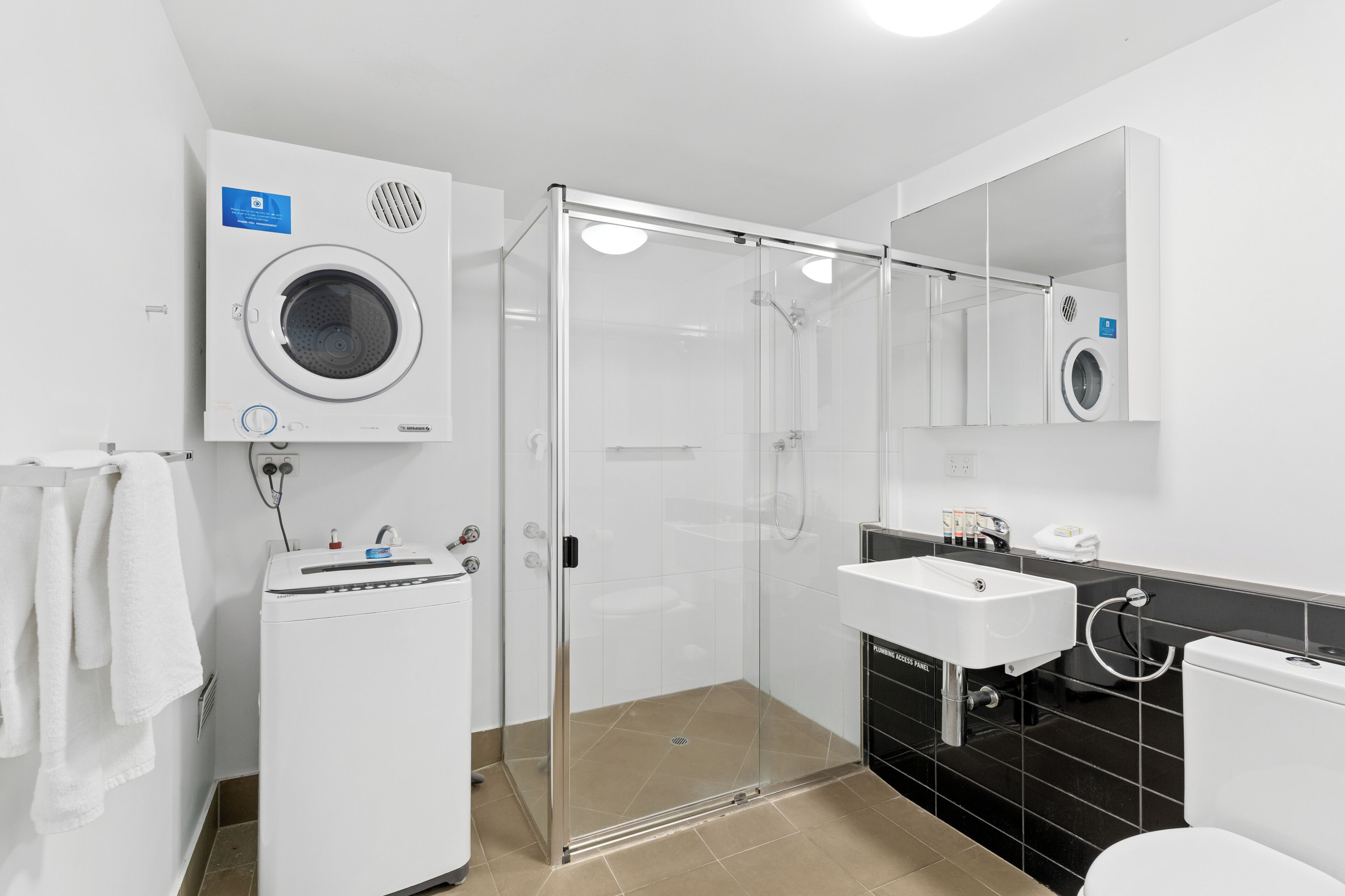 Ett modernt badrum med en duschavdelning med glasväggar, en inbyggd tvättmaskin, ett handfat och en toalett.