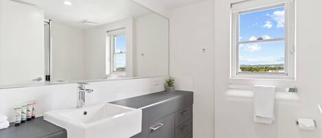 Un baño moderno con un espejo grande, un lavabo blanco, armarios grises, una ventana con vistas y un perchero para toallas.