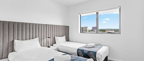 A hotel room with two beds, a ceiling fan, a large window with a city view, and a modern design.
