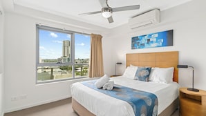 A hotel room with a bed, a ceiling fan, a window with a view, and a painting on the wall. - Direct Collective - Pavilion and Governor on Brookes (Bowen Hills)