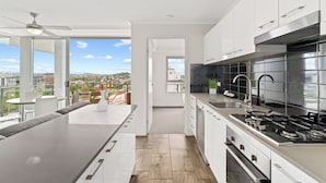 A modern kitchen with a large island, stainless steel appliances, and a view of the city. - Direct Collective - Pavilion and Governor on Brookes (Bowen Hills)