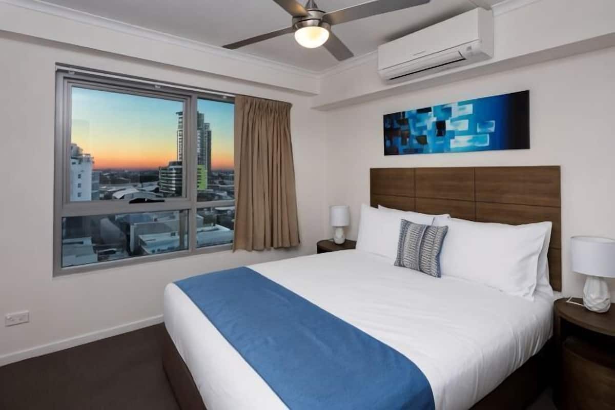 Una habitación de hotel con una cama grande, vistas a la ciudad, un ventilador de techo y un aire acondicionado.