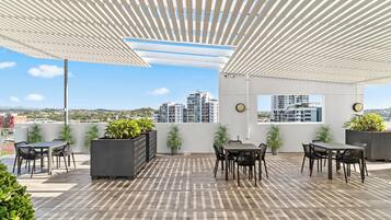 A rooftop patio with outdoor seating, potted plants, and a view of city buildings.