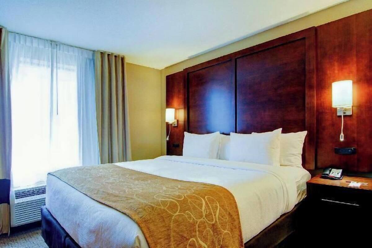 A hotel room with a large bed, a wooden headboard, two bedside lamps, and a nightstand with a phone.