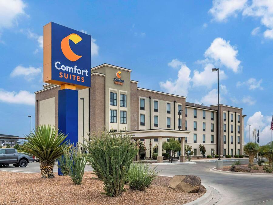 Un hotel Comfort Suites con un llamativo letrero azul, fachada de ladrillo y un área de entrada cubierta.