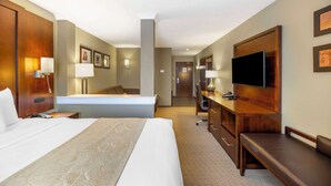 Habitación de hotel con una cama grande, un escritorio con televisor de pantalla plana, una silla, una lámpara de escritorio y un televisor montado en la pared.
