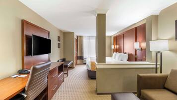A hotel room with a desk, chair, bed, and a TV mounted on the wall.