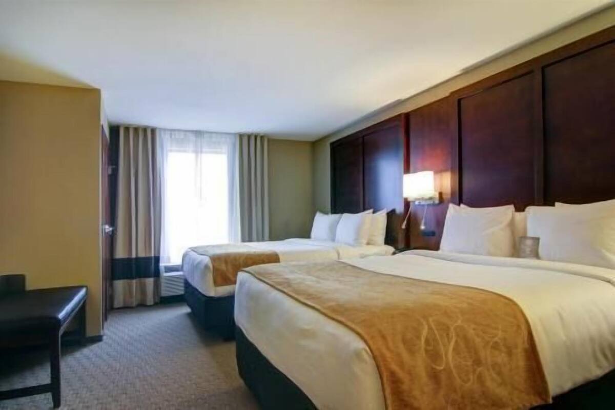 A hotel room with two beds, a desk, and a large window with curtains.