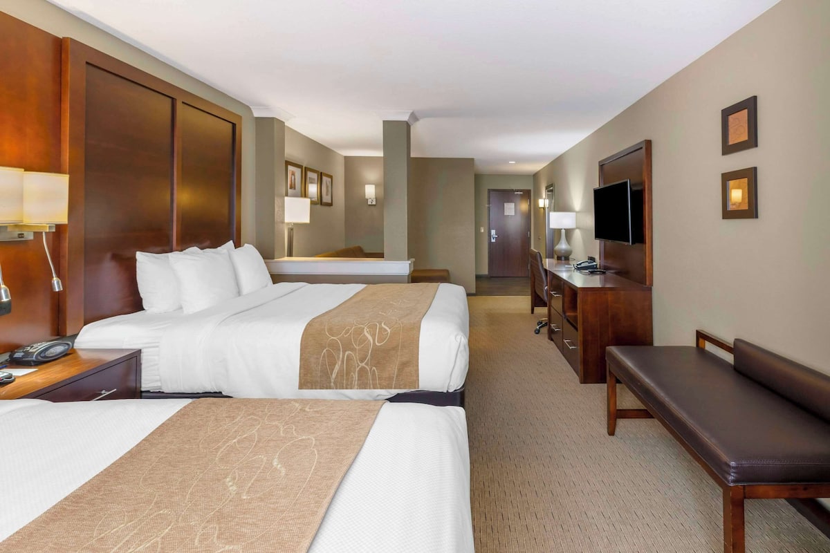 A hotel room with two beds, a desk, a chair, a TV, and a door leading to another room.