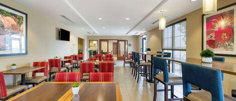 A spacious restaurant with multiple dining areas, including booths and tables. There are ceiling lights and large windows providing natural light.
