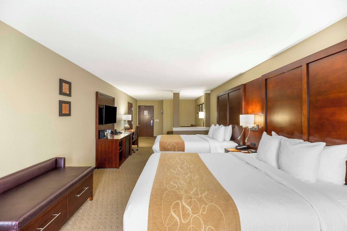 A hotel room with two beds, a desk, a chair, a television, and a bathroom.