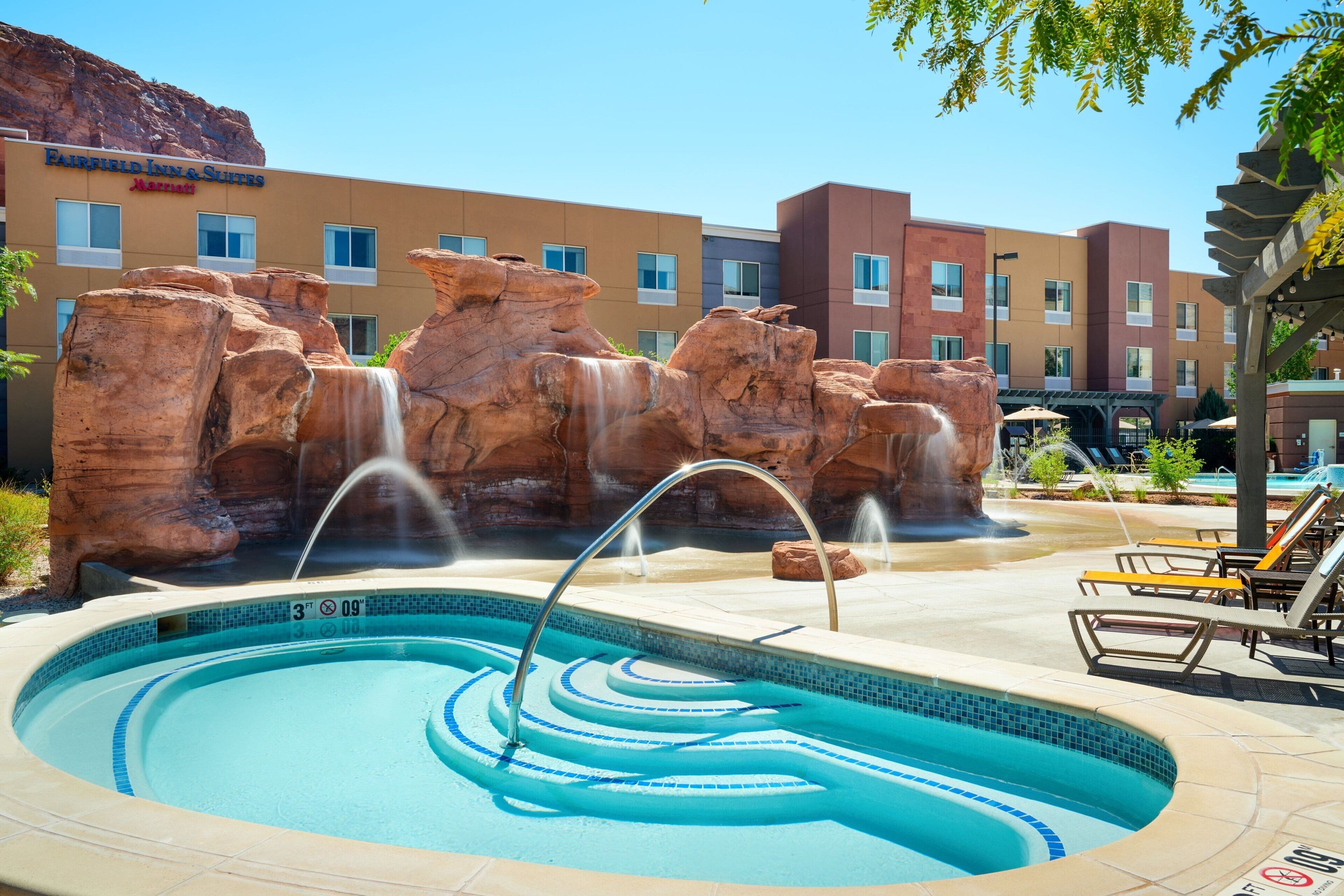 Un hotel con piscina que cuenta con una cascada de rocas y sillas de descanso.