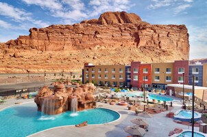 Un hotel con zona de piscina que incluye una cascada, asientos al aire libre y montañas al fondo.