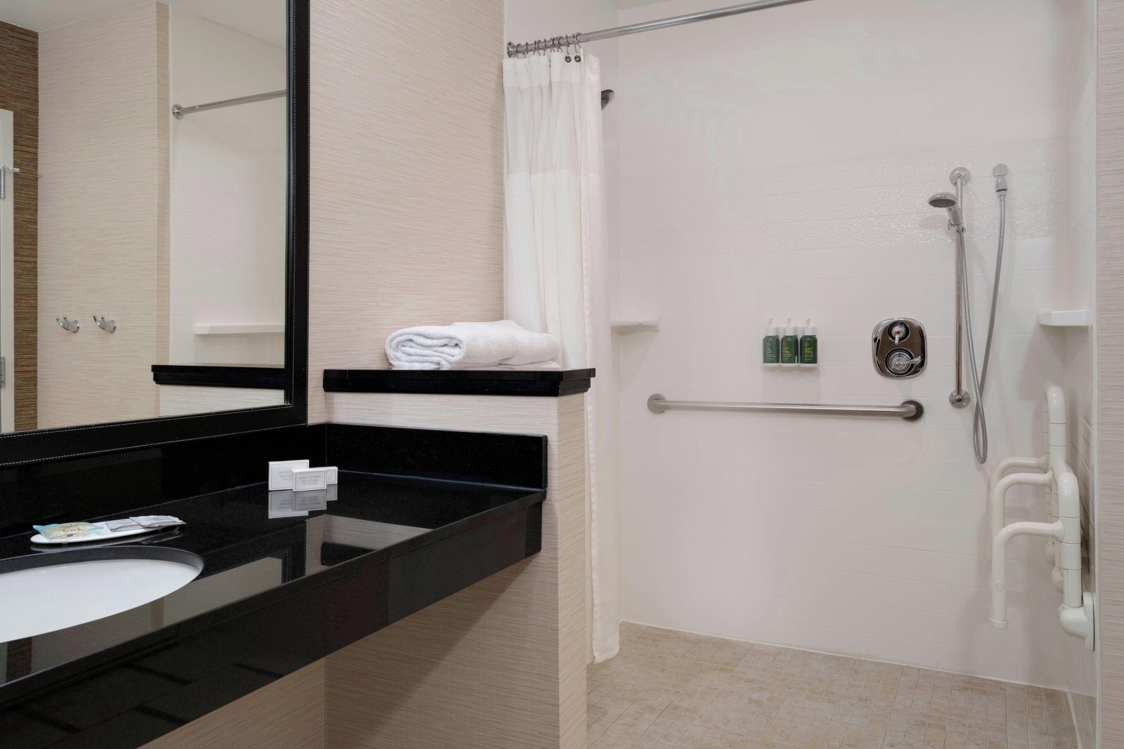 Ein modernes Badezimmer mit schwarzem Waschtisch, weißem Waschbecken, einem großen Spiegel, einer Dusche mit Glastür und einer Haltestange.