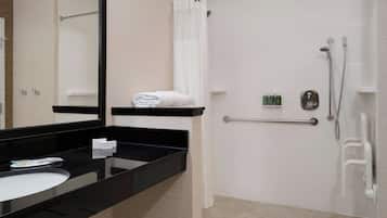 Un baño moderno con encimera negra, lavamanos blanco, espejo grande, ducha con puerta de cristal y barra de apoyo.