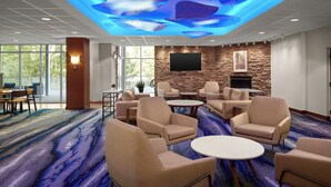 A conference room with beige chairs and tables, a stone accent wall, a flat-screen TV, and a ceiling with a blue abstract design. - Fairfield Inn & Suites by Marriott Rehoboth Beach (Rehoboth Beach)