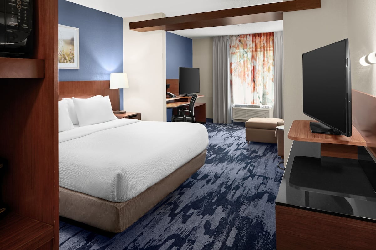 A hotel room with a large bed, a desk with a computer, a television, and a window with curtains.