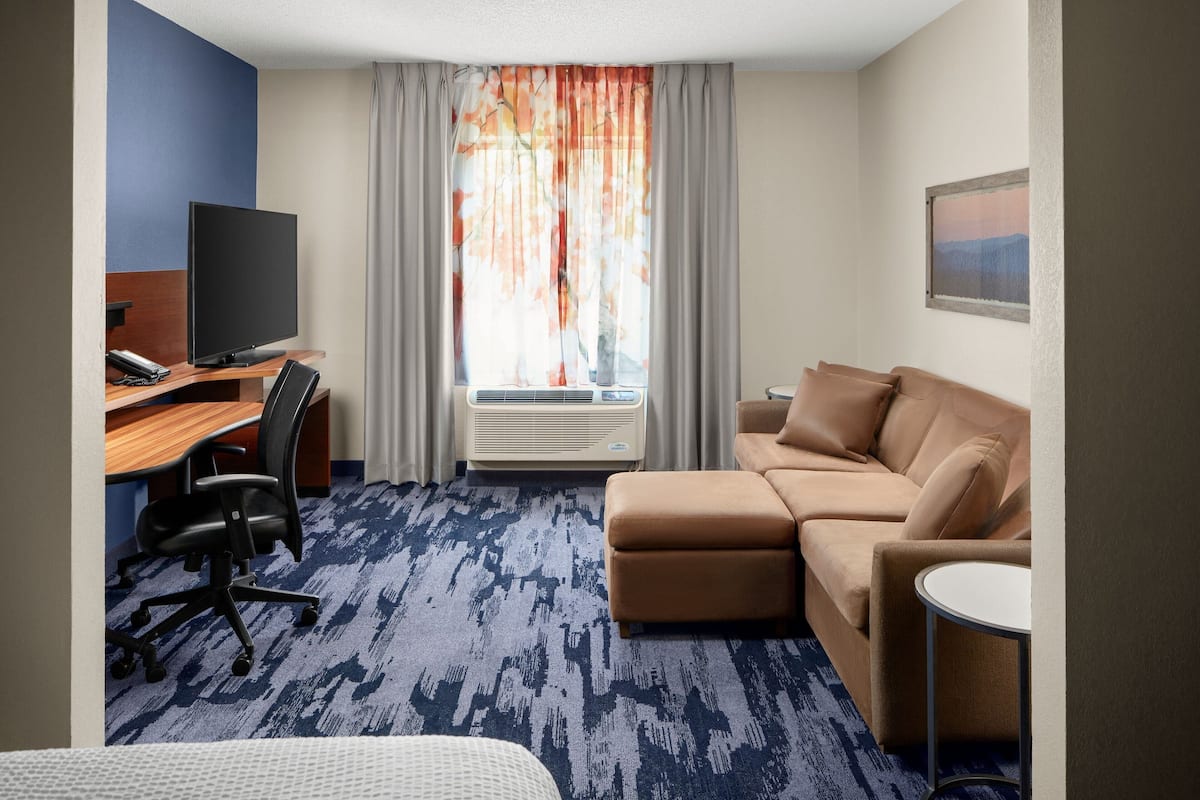 A hotel room with a desk, chair, sofa, and a small table.