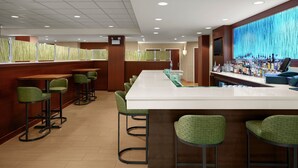 A bar area with a long counter, multiple stools, and a television screen. - Fairfield Inn & Suites by Marriott Rehoboth Beach (Rehoboth Beach)