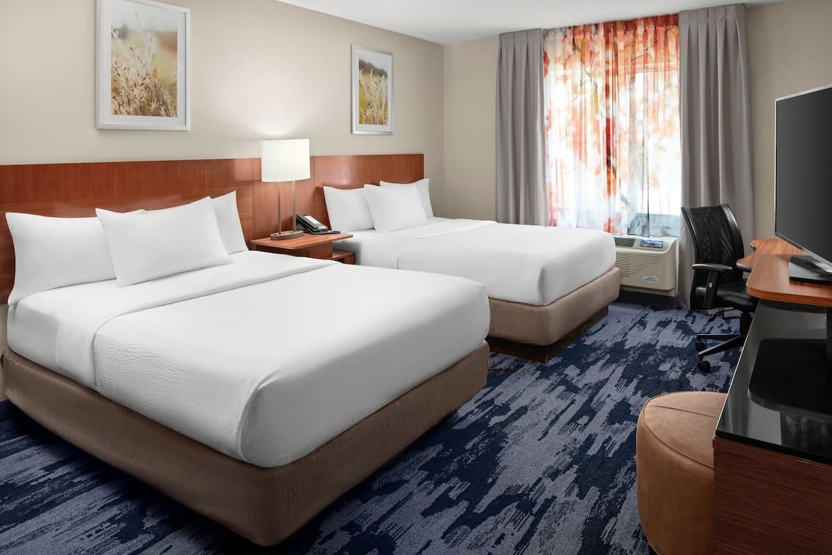 A hotel room with two beds, a desk with a chair, a television, and a window with curtains.