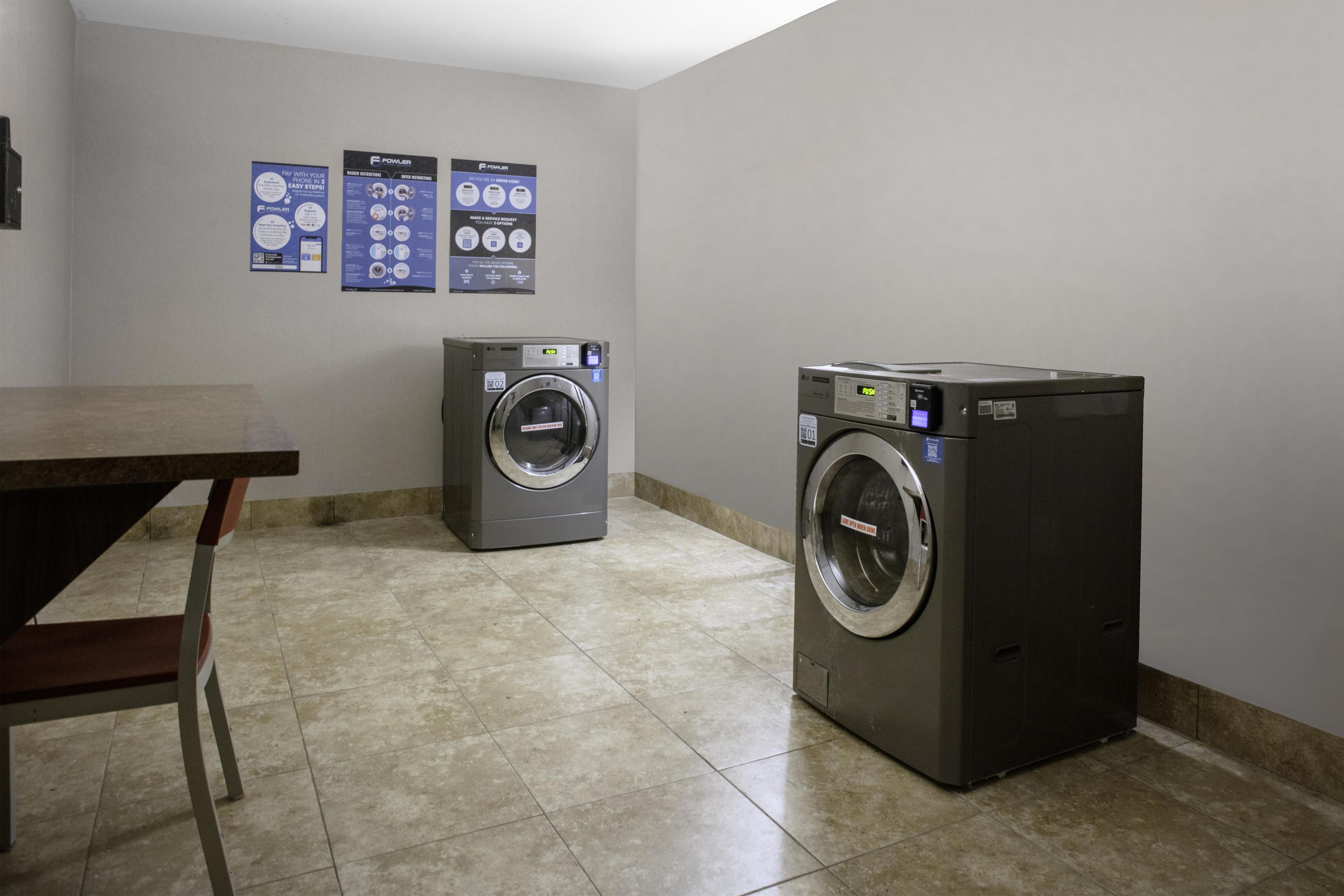 A laundry room with two front-loading washing machines, a table, and informational posters on the wall.