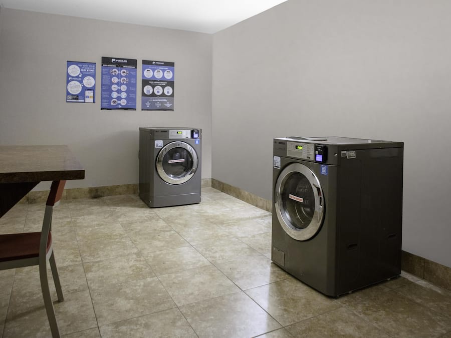 A laundry room with two front-loading washing machines, a table, and informational posters on the wall.