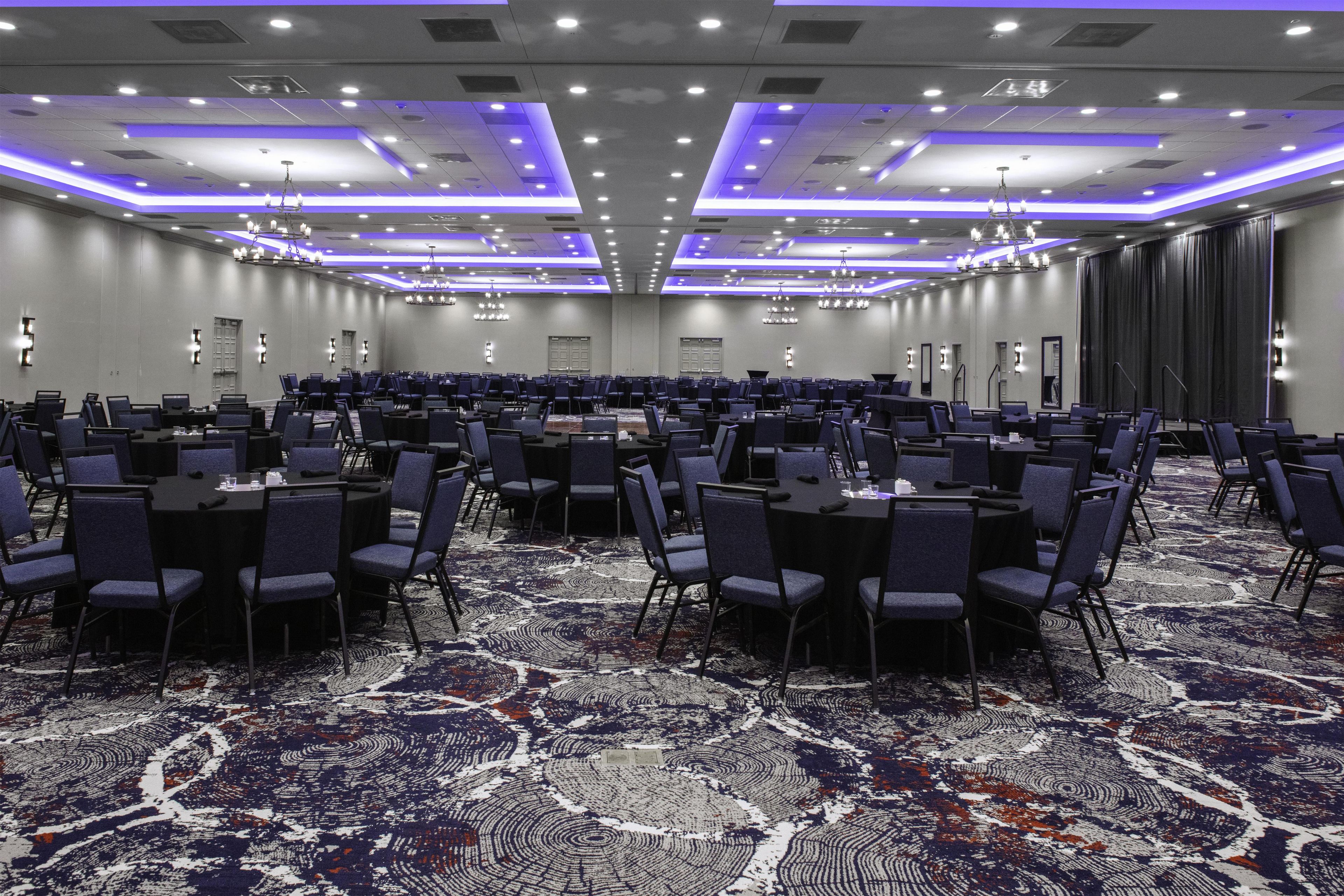 A large conference room with rows of tables and chairs, a patterned carpet, and modern lighting fixtures.