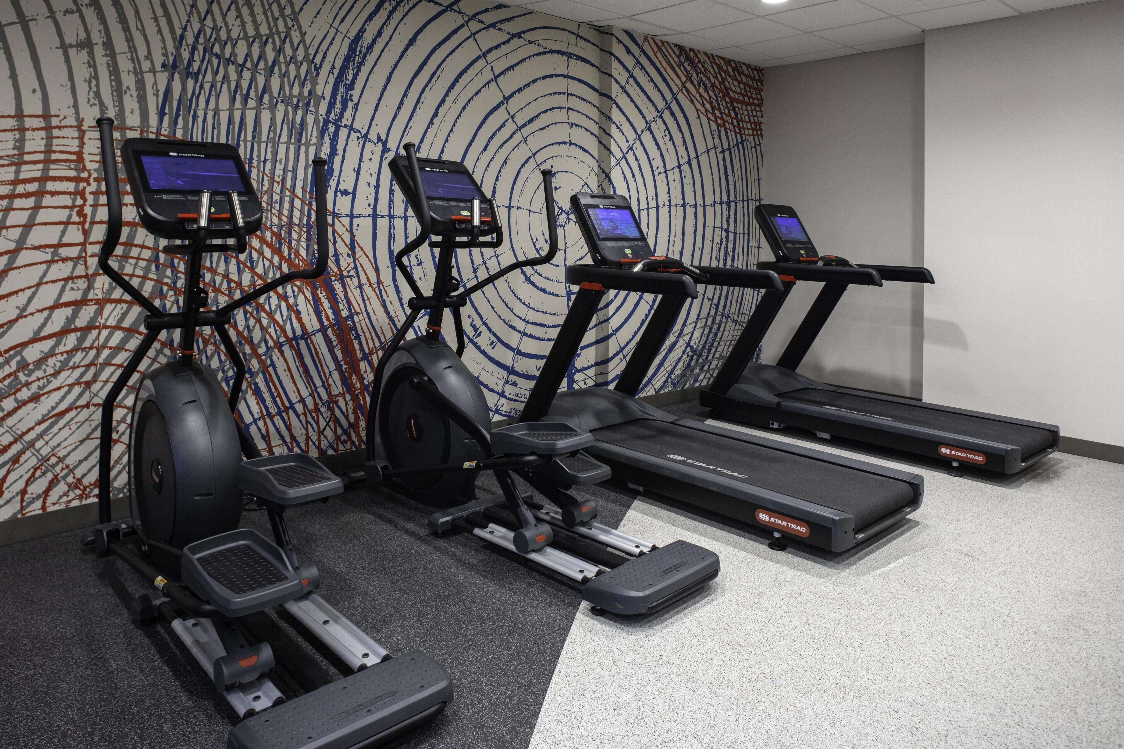 Un gimnasio con cintas de correr, elípticas y una bicicleta estática.