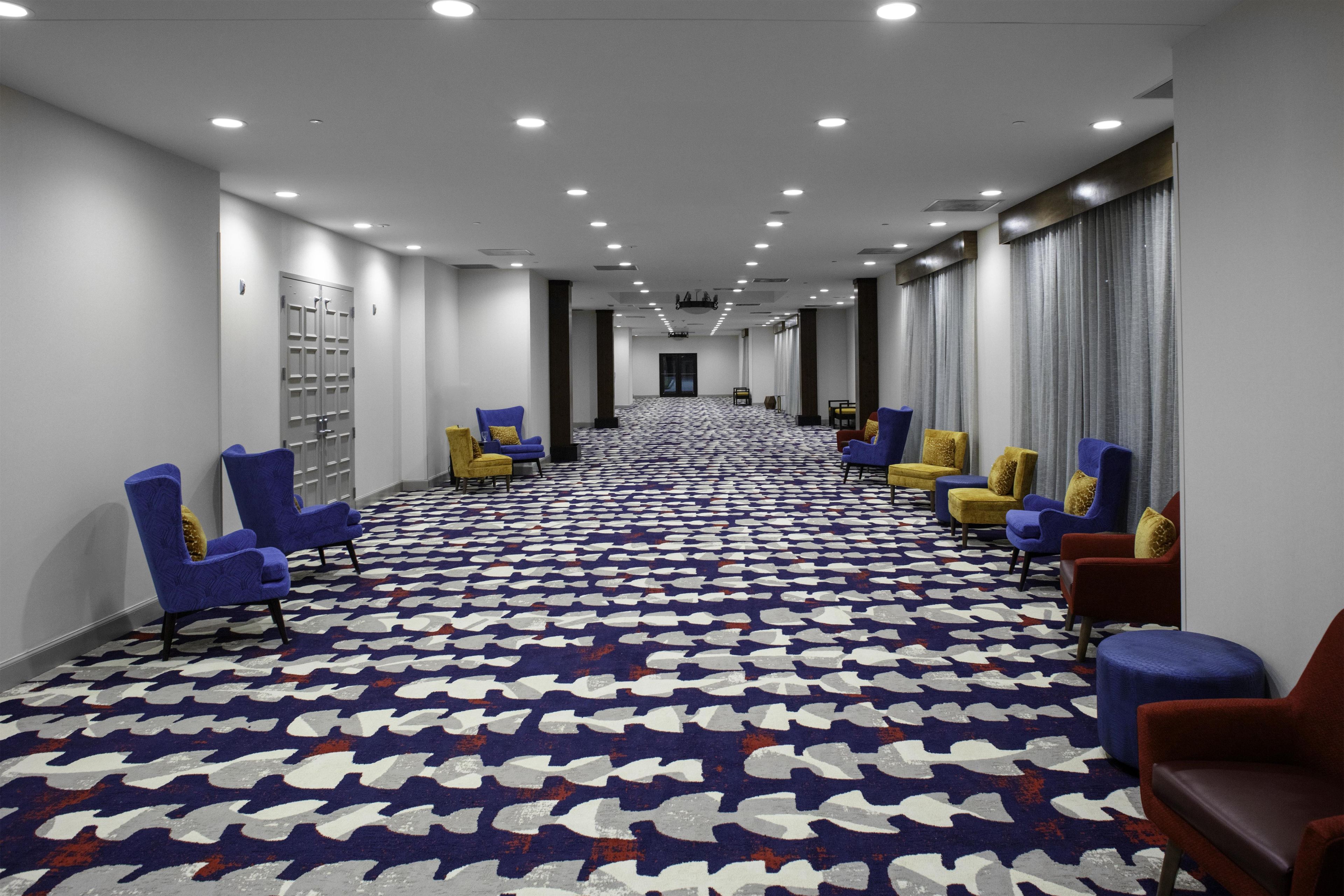 A hotel corridor with rows of chairs, a patterned carpet, and a long hallway.