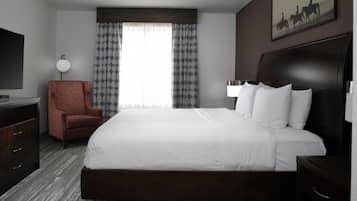 A hotel room with a large bed, a desk, a chair, a TV, and a painting on the wall.