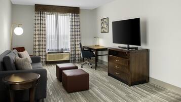 Una habitación de hotel con sofá, escritorio, televisor, silla y cómoda.