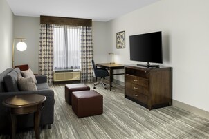 Una habitación de hotel con sofá, escritorio, televisor, silla y cómoda.