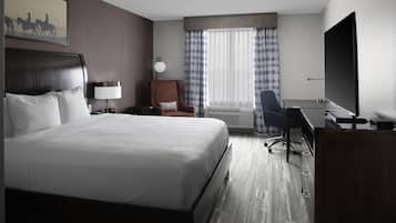 A hotel room with a large bed, a desk, a chair, a television, and a window with curtains.